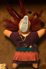 a small doll-like fetish with a headdress of feathers, beaded necklace, mask and dress made of leather.